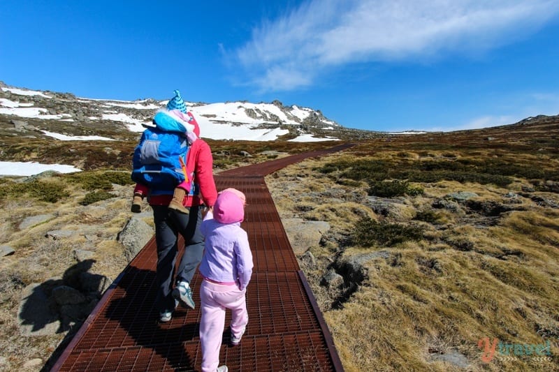 family hiking up iron boardwalk amoungst snowy mountains 