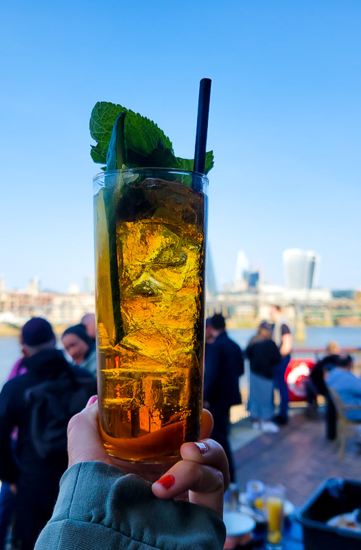 hand holding pimm's and lemonade with views of london in background