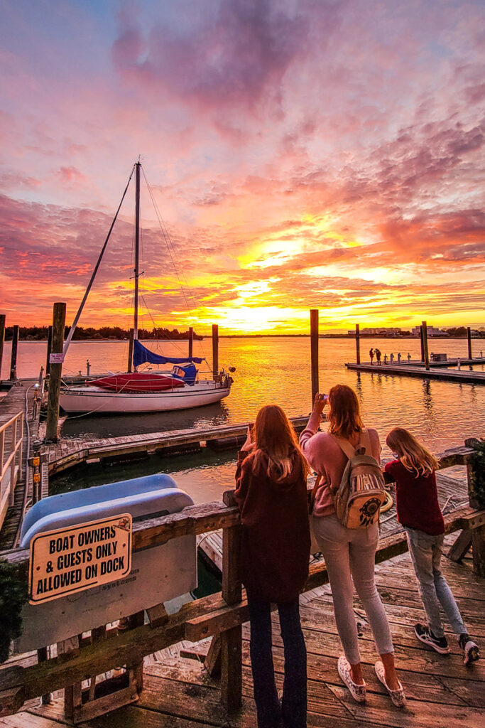 people standing on a board walk watching the sunset