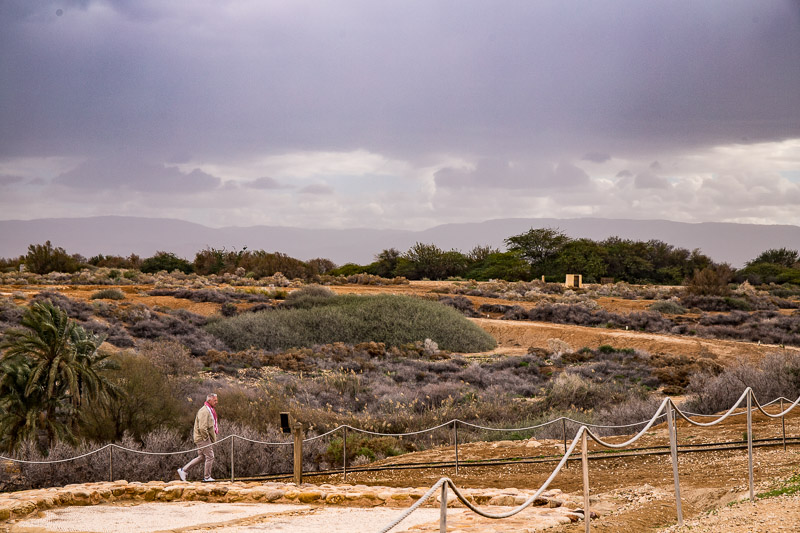 man walking through a desert landscape with dark clouds