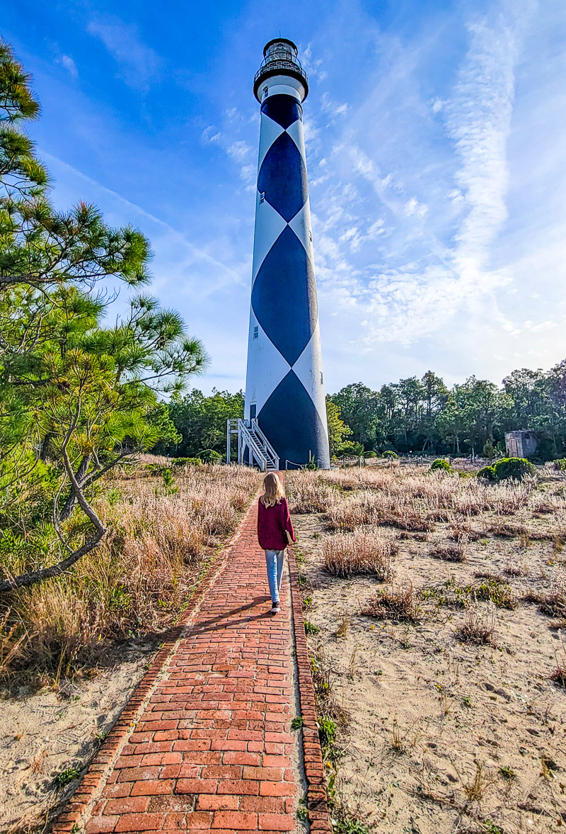 girl walking in front of a black and white diamond lighthouse