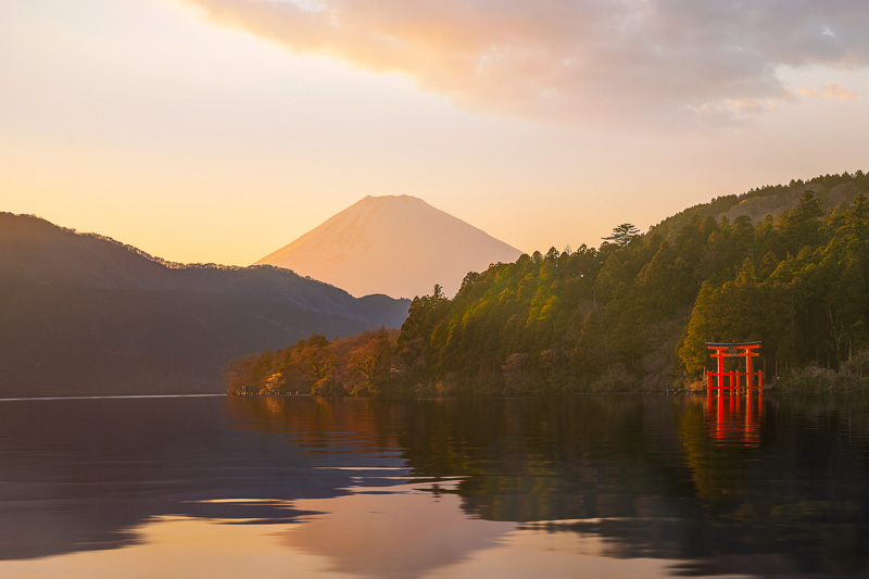 red shrine by a lake framed by trees adn mt fui in the background