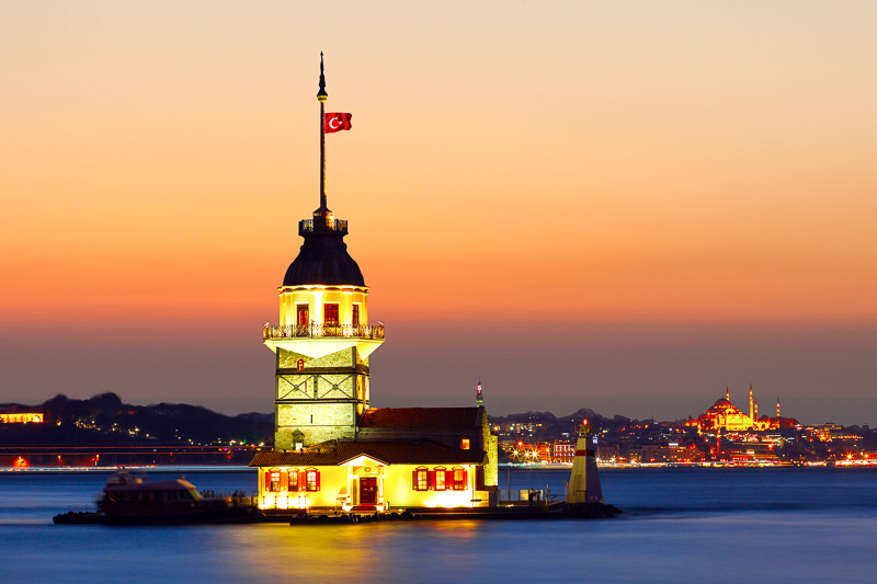 short tower with Turkish flag flying in the middle of the river at sunset