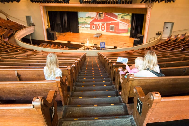 family on tour at the Ryman Auditorium sitting on pews looking at stage