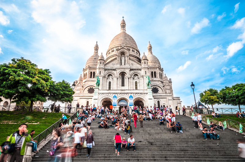 People sitting on stairs leading up t Sacre Coeur Basilica in summer day.