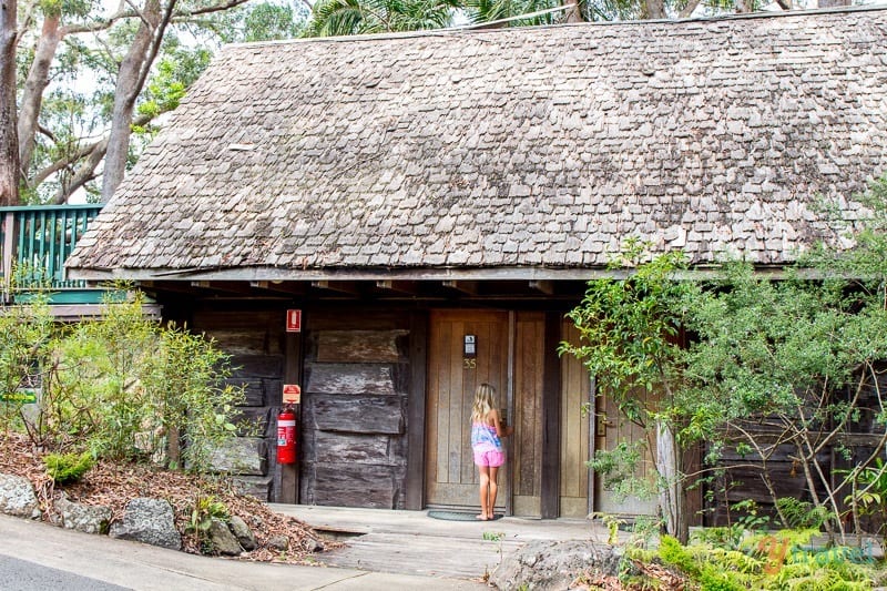 little girl opening the door of a wooden cottage