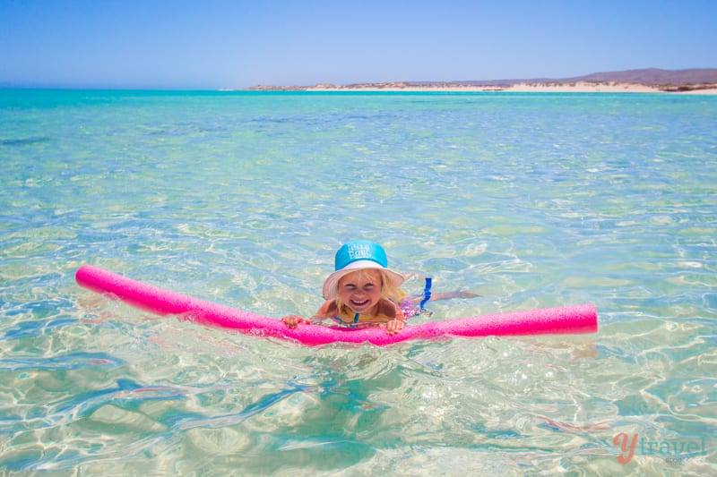 girl swimming with float in sandy bay