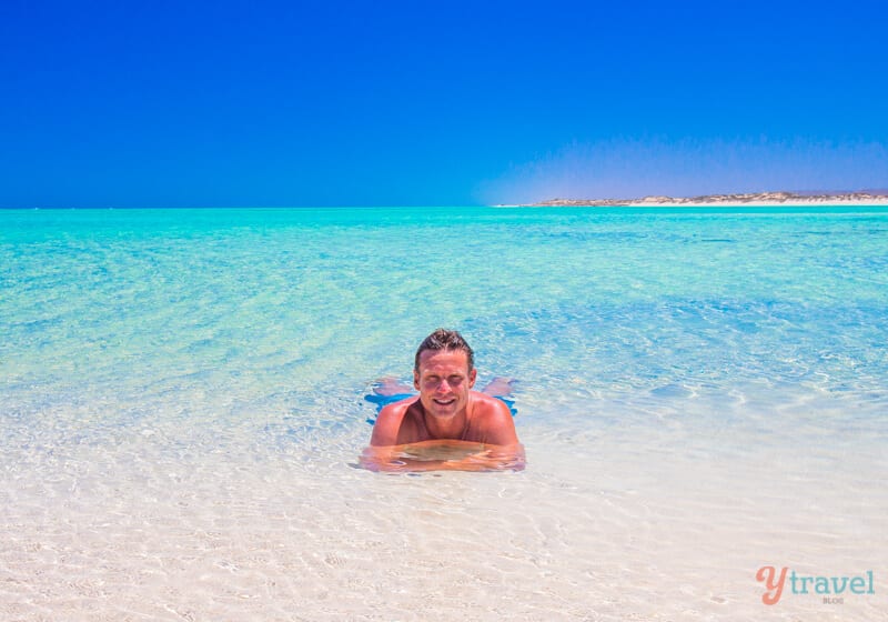 man sitting in crystal clear water at Sandy Bay