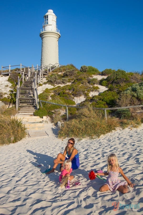 people sitting on a beach in front of a lighthouse