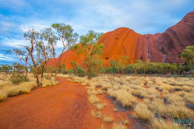 A dirt road leading towards a big red rock