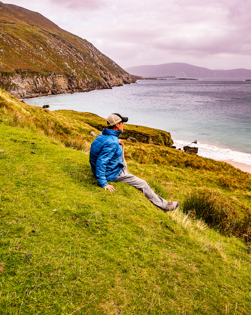 Man sitting on a grass hill overlooking a beach