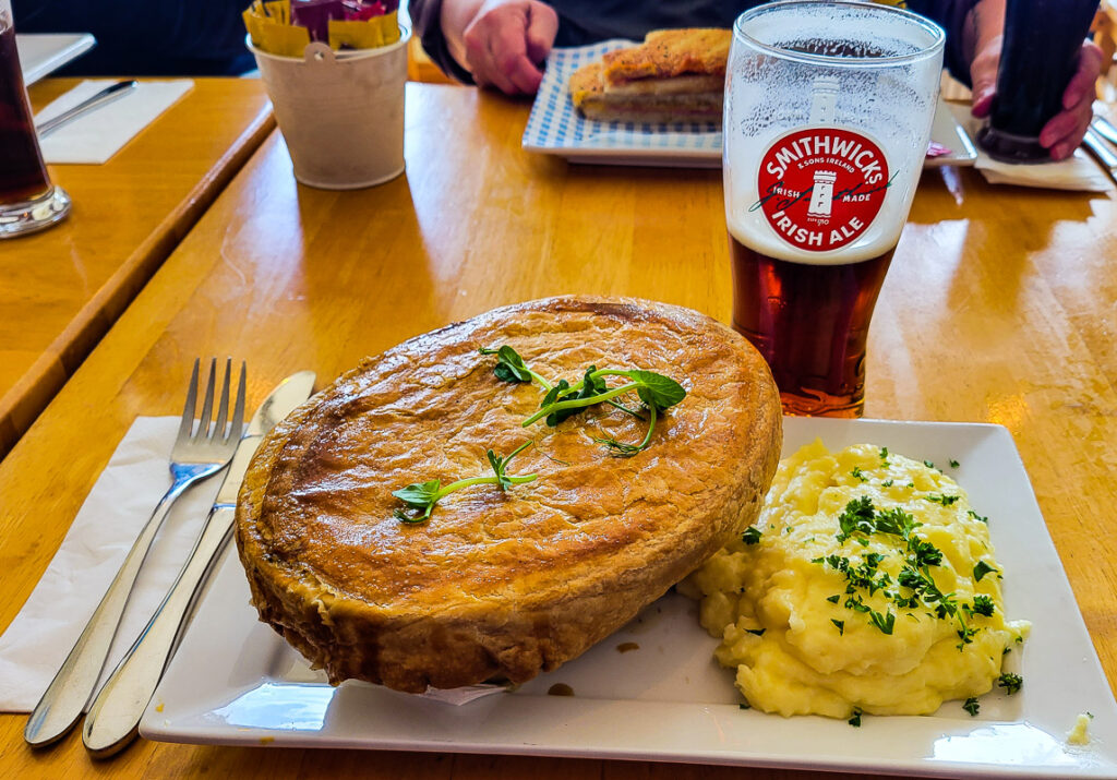 A large pastry of pie on a plate with potato and a glass of beer