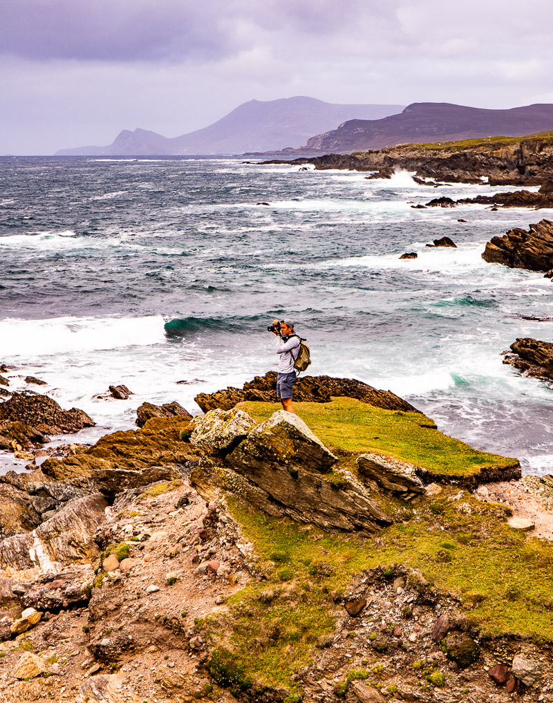 A man standing on rocks taking photos of the ocean