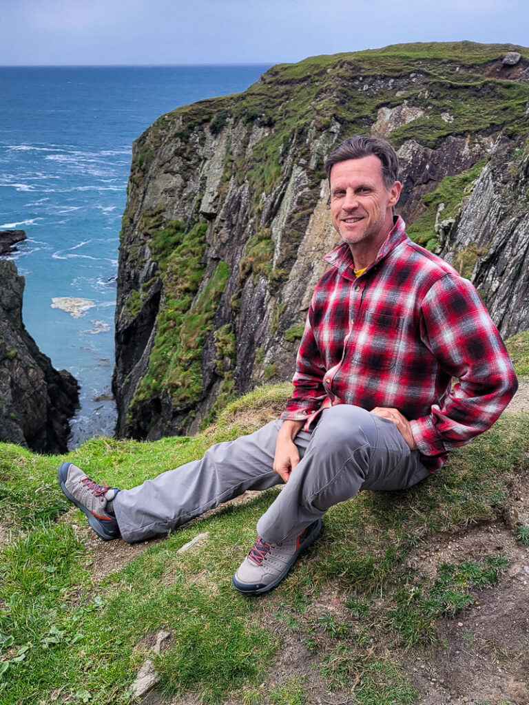 Man sitting on grass overlooking a rock formation and ocean