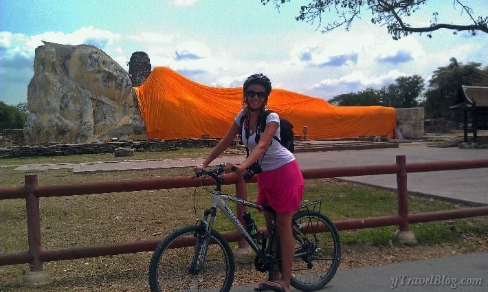 woman sitting on bike in front of giant lying buddha in a monks robe 