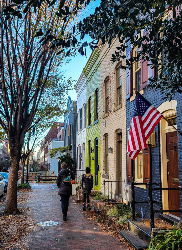 Mother and daughter walking along a sidewalk with American flag and townhownes