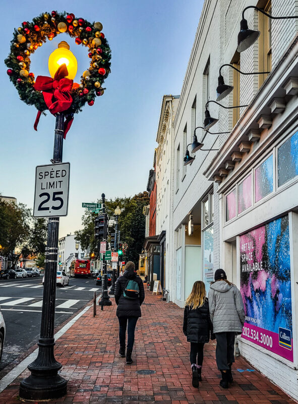 A mom and two daughters walking along a city street with Christmas decorations