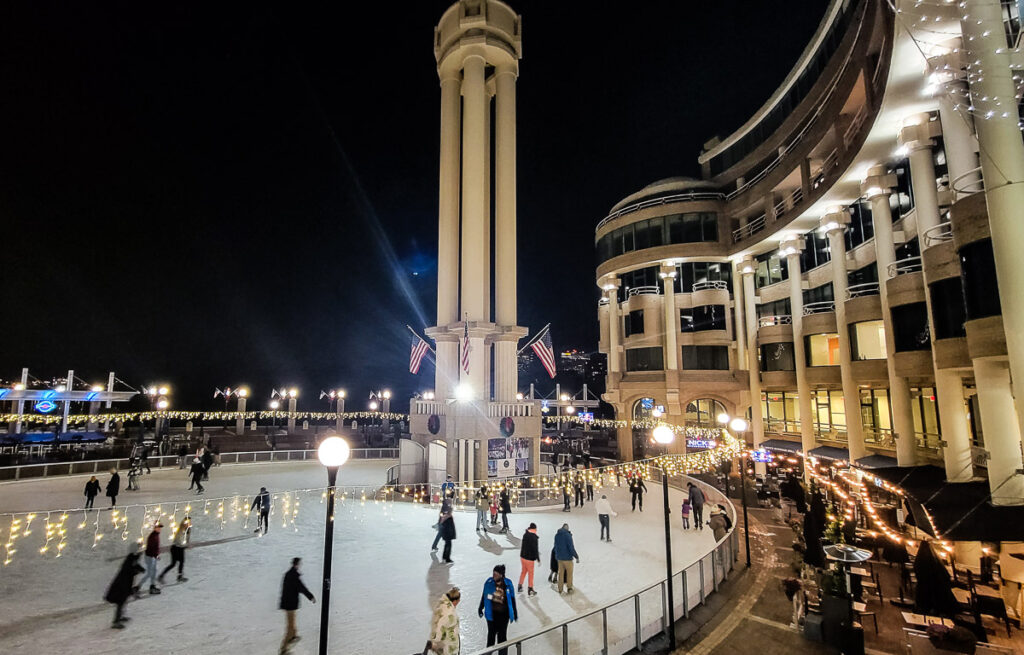 People ice skating inside a rink surrounded by buildings