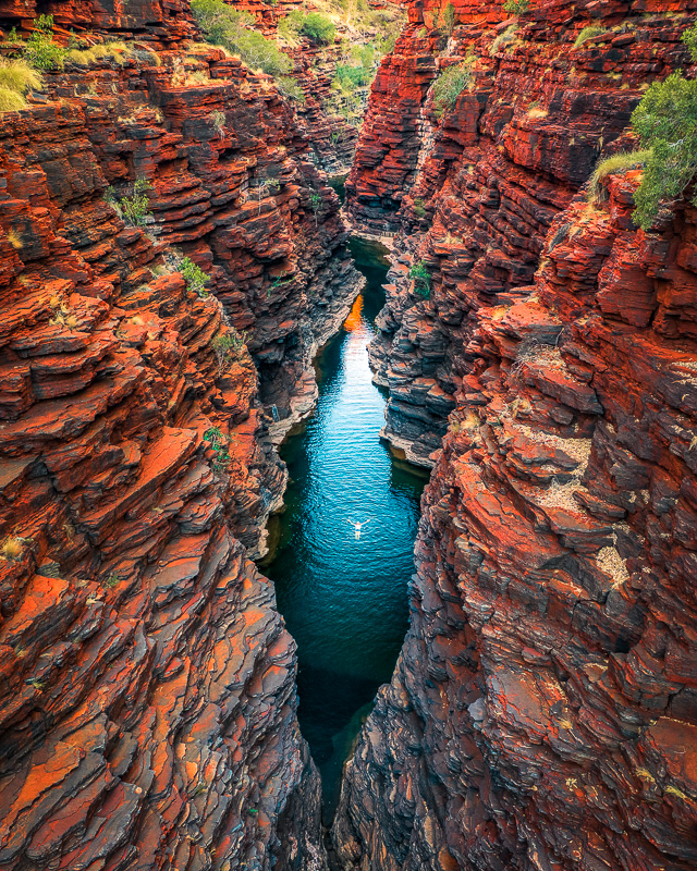 person swimming in pool surrounded by wavy red and orange rock gorge walls