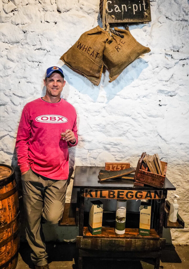 Man standing against a wall holding a glass of Whiskey