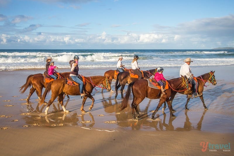 group of people horseback riding on the beach