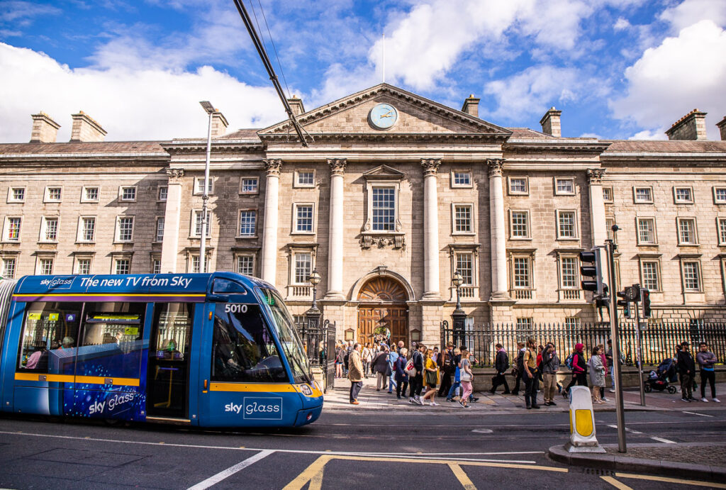 A light rail passing by people and a college in Dublin