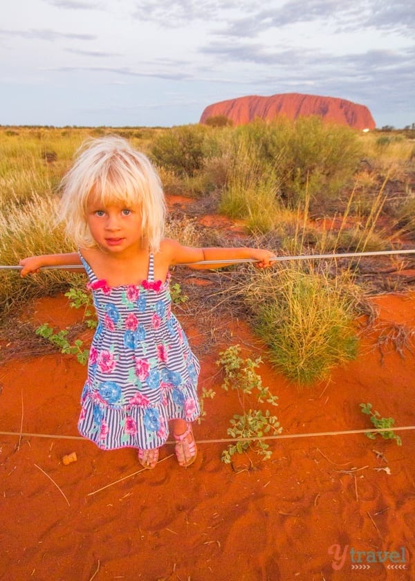 little girl standing on a rope fence in front of ayers rock