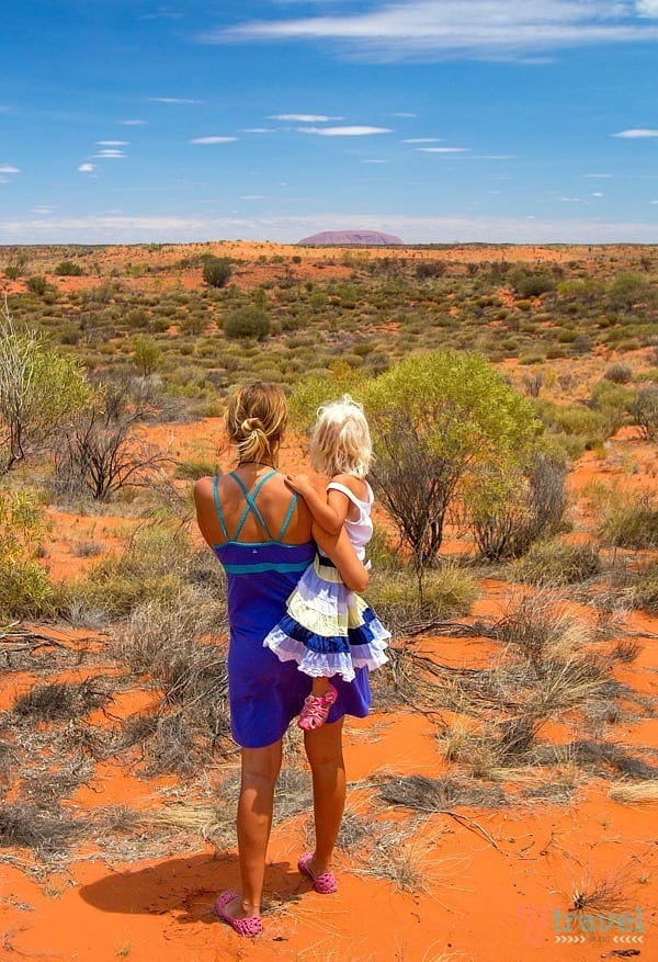 woman holding child looking at Uluru on the horizon 