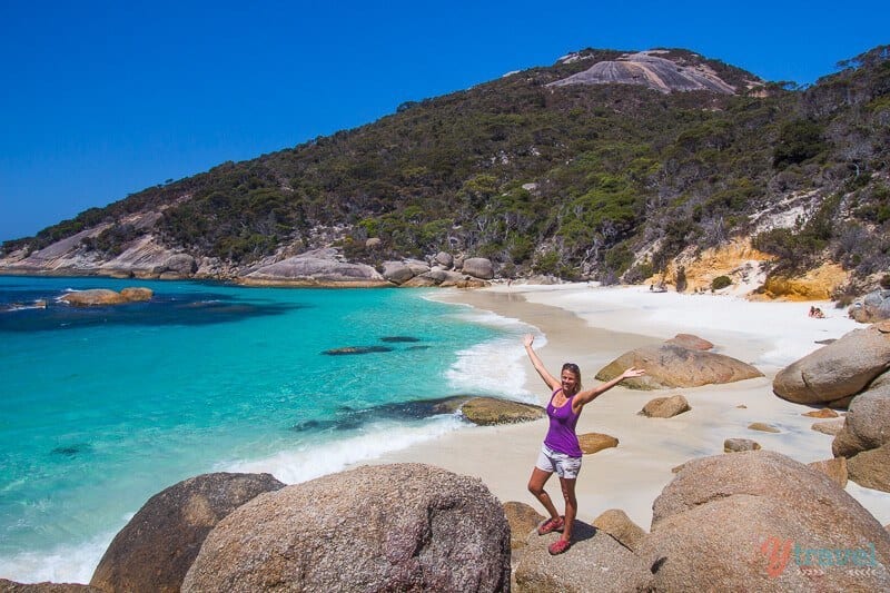 woman standin gon rock with hands in the air on Waterfall Beach, Albany