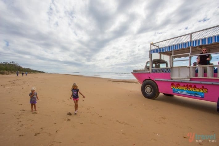 girl walking on the beach next to a pink truck