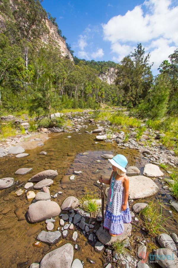 girl standing in a river surrounded by trees and mountains