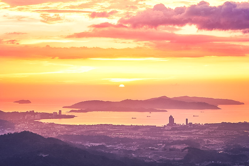 View of silhouette landscape with Kota Kinabalu city against islands at golden sunset.  Sabah state, Malaysia.