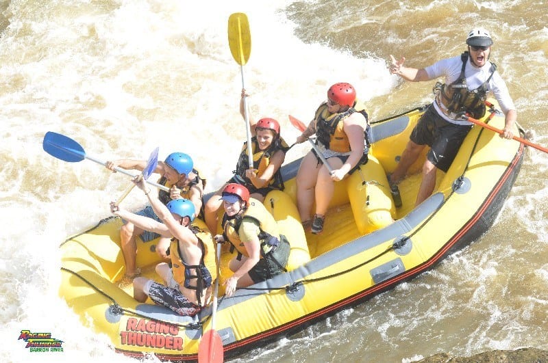 people in rafting boat waving paddles in the air 