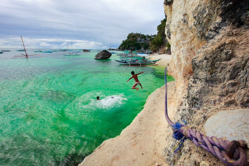 Boys jumping from cliff into turquoise ocean waters