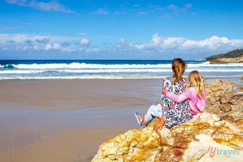 woman and girl hugging on rock on beach