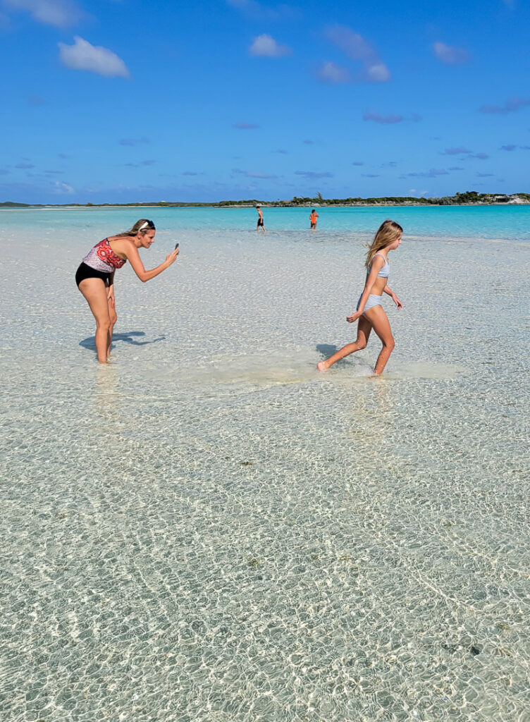 Mom taking photo of daughter running in shallow water at the beach