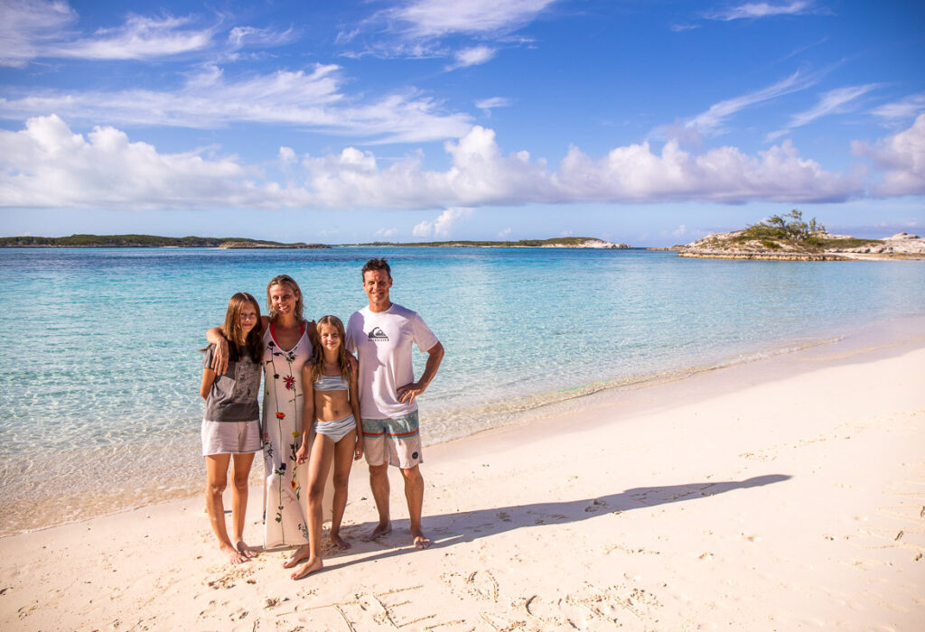 Family of four getting a phot taken on the beach with beautiful blue water behind them