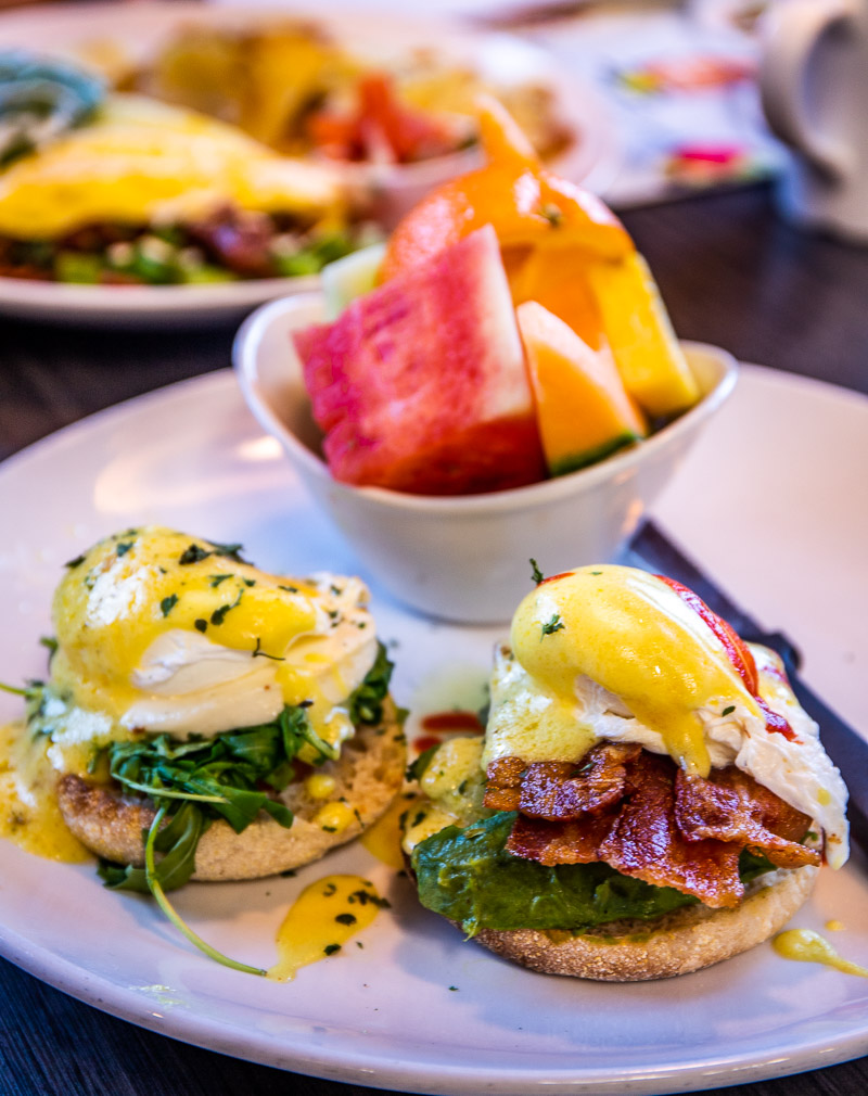 Two eggs benedict plus fruit on a plate