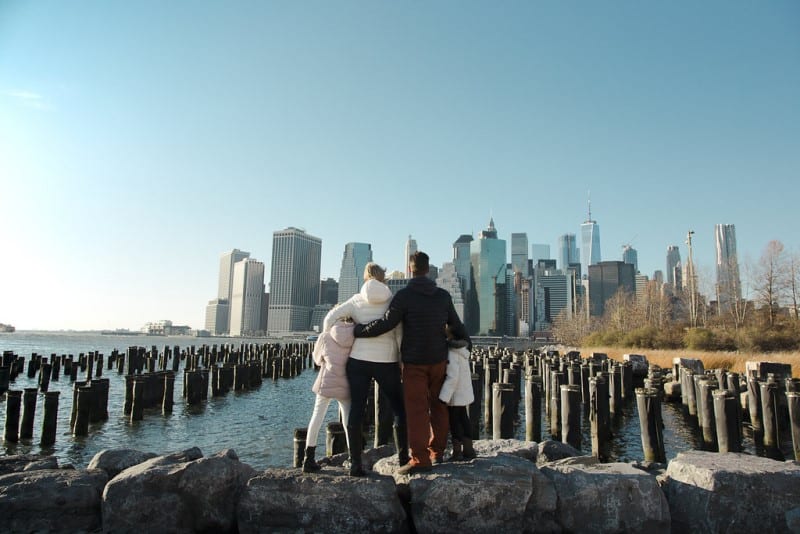 family cuddling looking at manhattan skyline from brooklyn bridge park