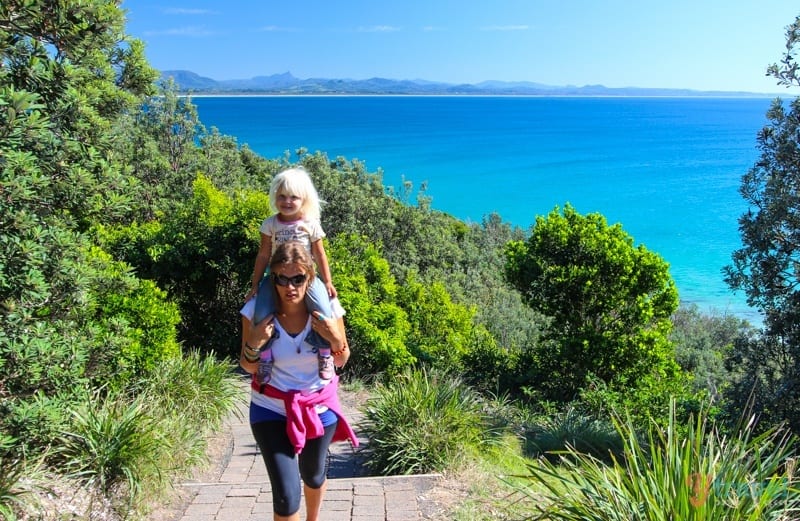 woman walking up a mountain while carrying a kid on her shoulders