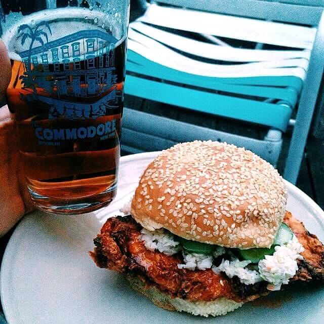 Spicy chicken sandwiches and pint of beer on table at The Commodore