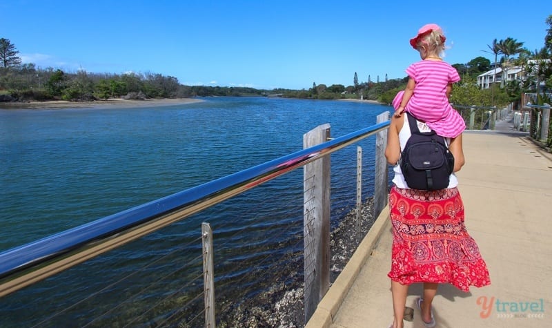 woman carrying a kid on her shoulders while walking on a bridge