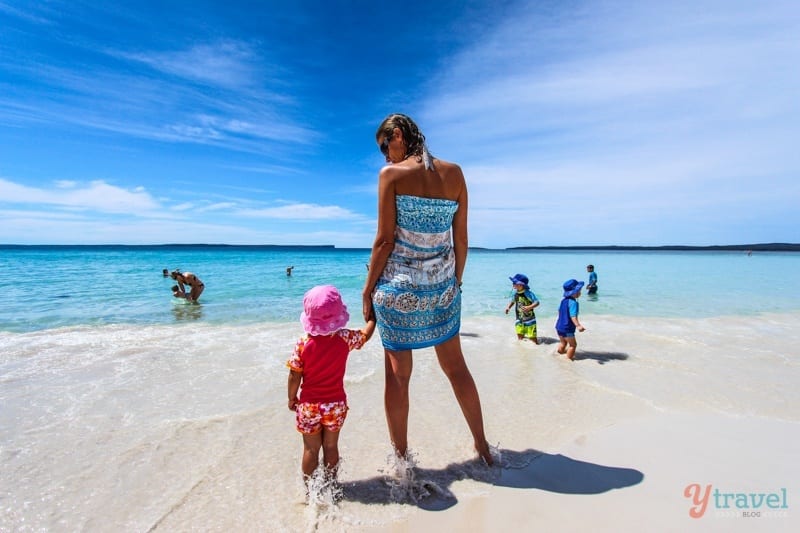 a woman holding a childs hand on the beach