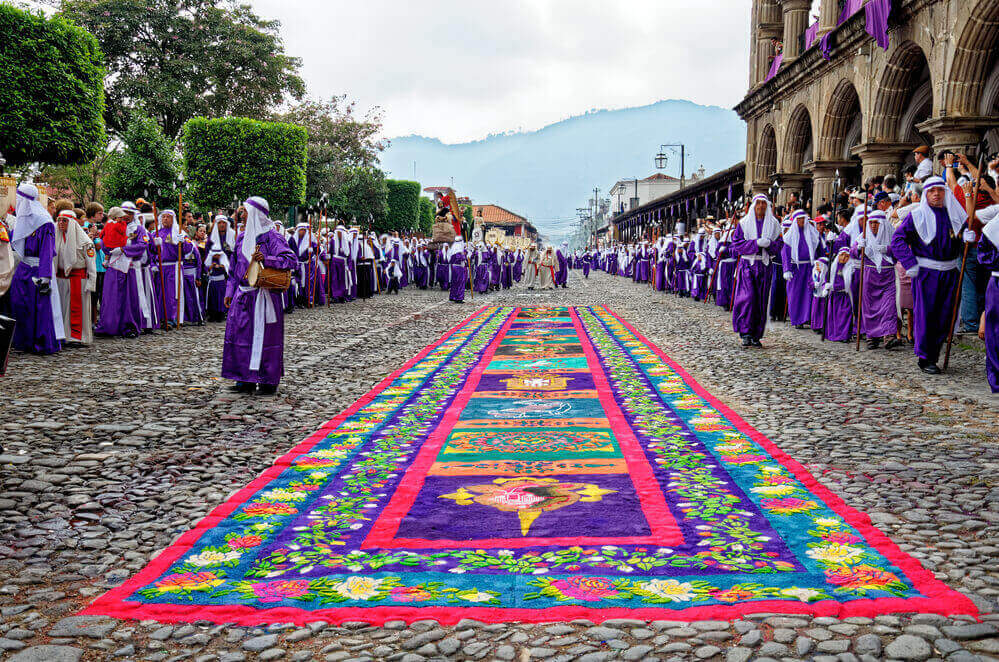 people dressed in purple robes lining the street covered in chalk art Semana Santa