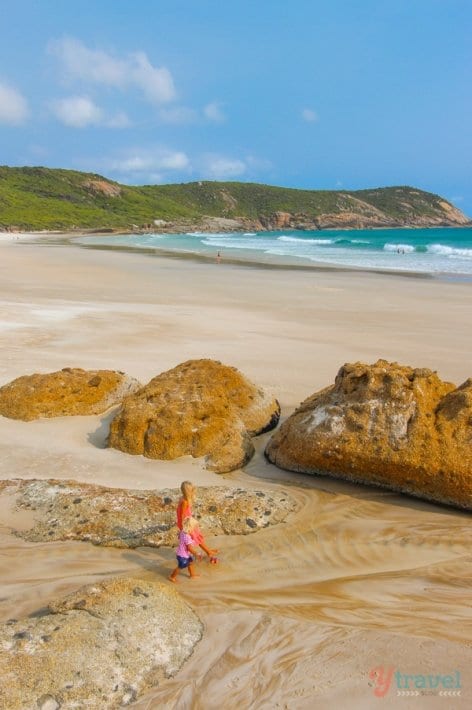 girls walking past large rocks on the beach