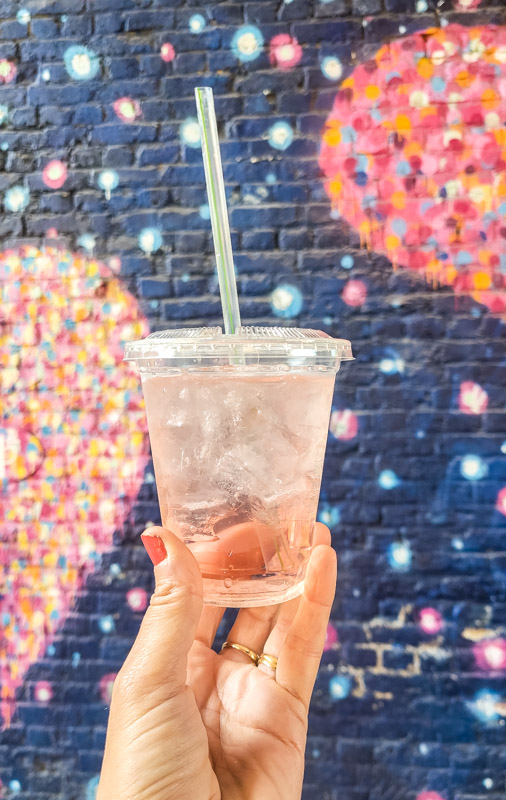 hand holding cup of peach prosecco in front of colorful heat mural