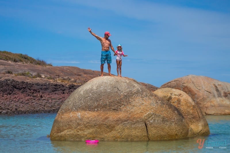 people standing on top of a boulder in the ocean