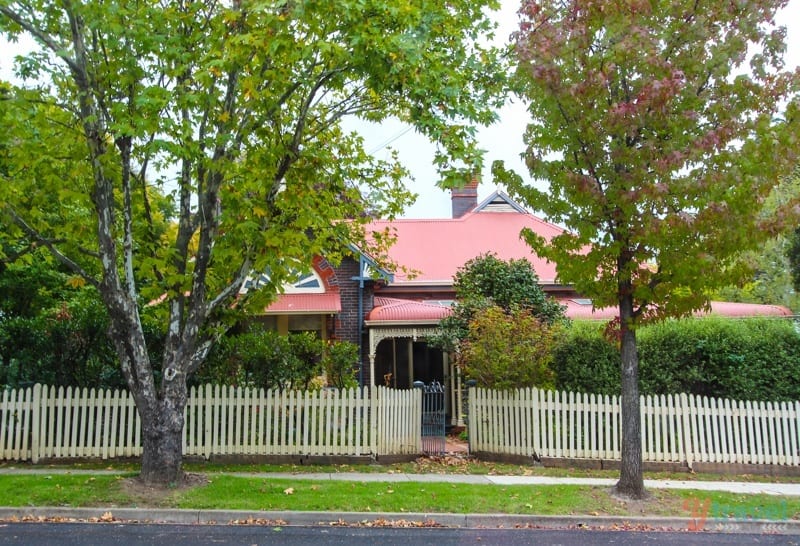 red roofed Heritage Home behind white picket fence