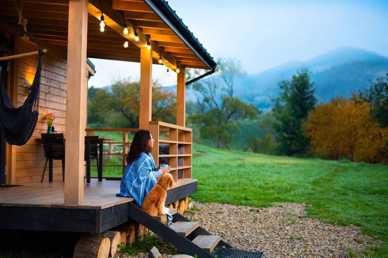 a woman sitting with her dog near a cabin in the woods