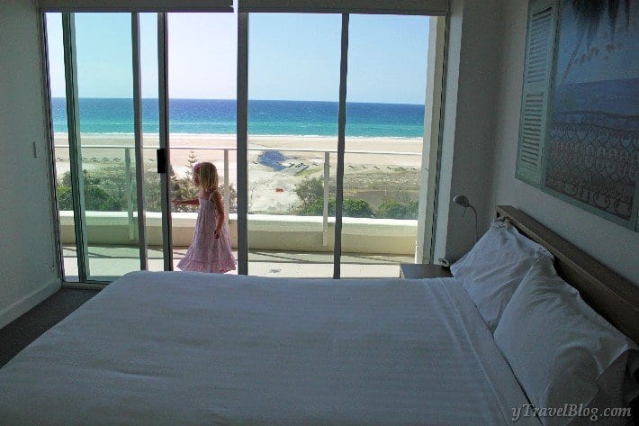 bed in apartment room with glass door sand view of girl on balcony and beach